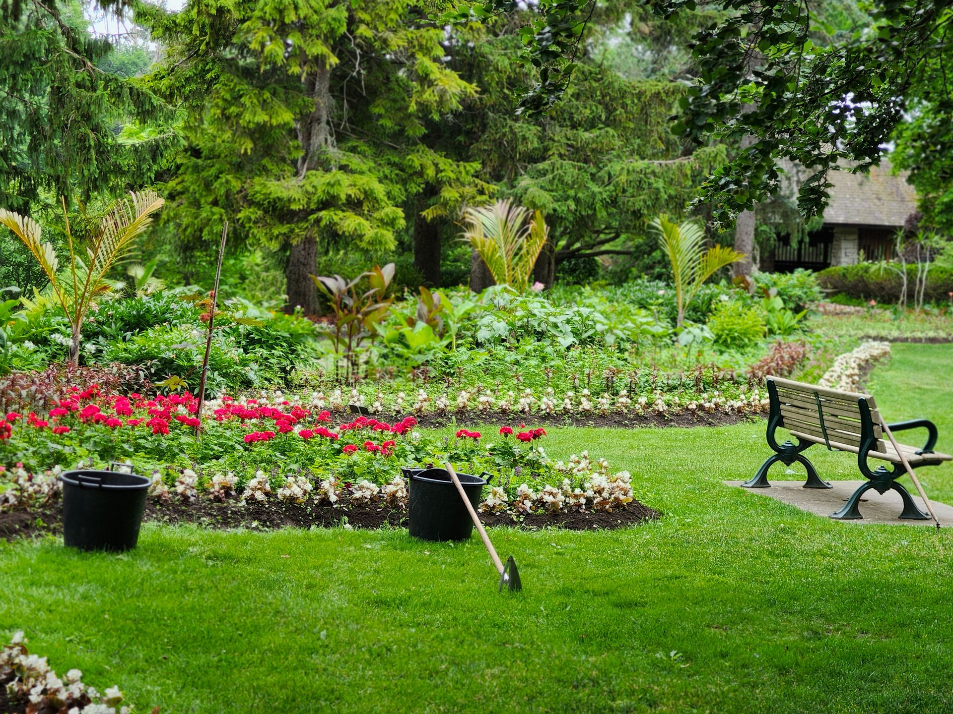 Tranquil park scene featuring lush greenery, a flower garden, and an empty bench.