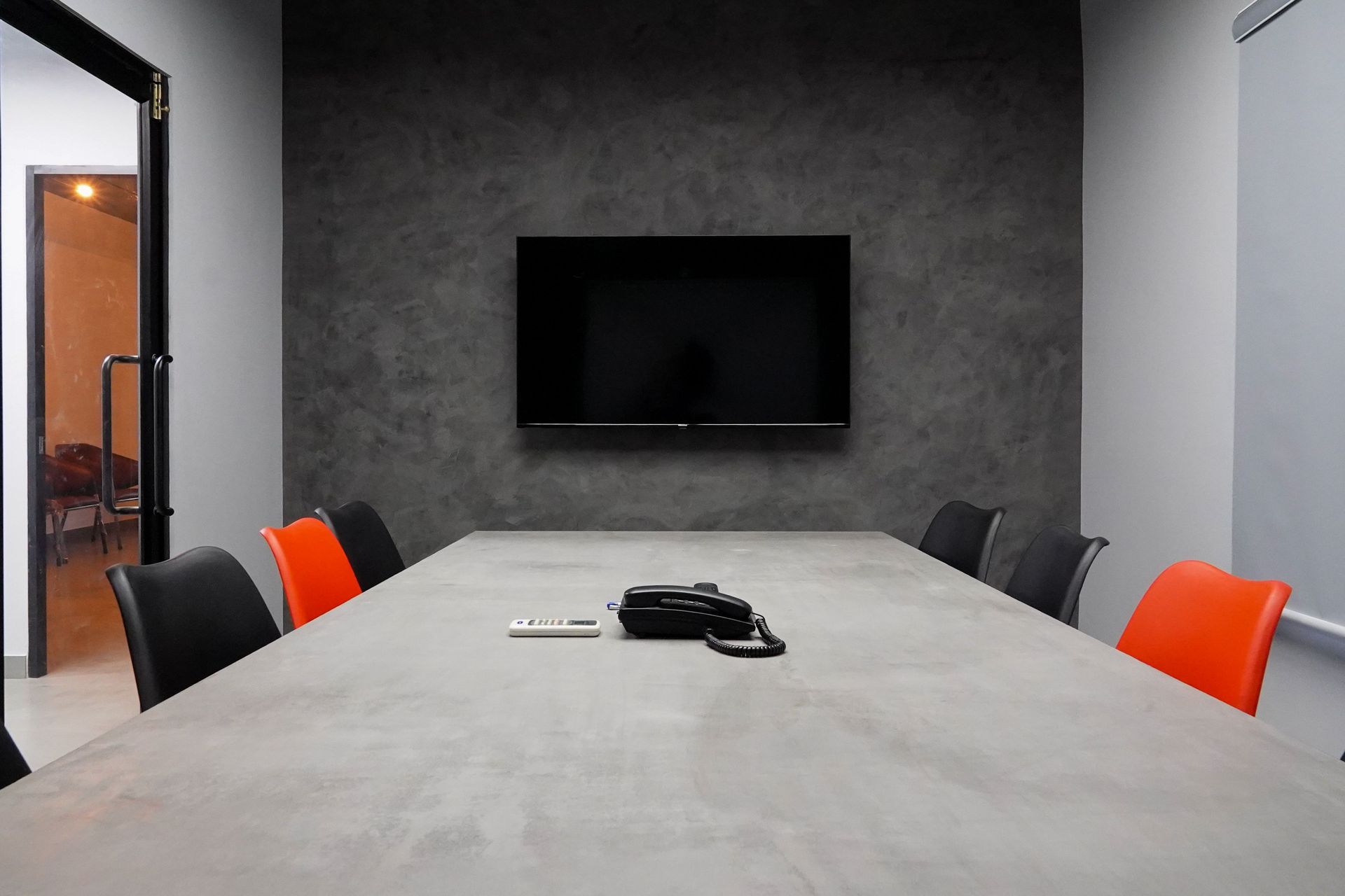 Sleek conference room featuring a large table, black and red chairs, and a wall-mounted TV.