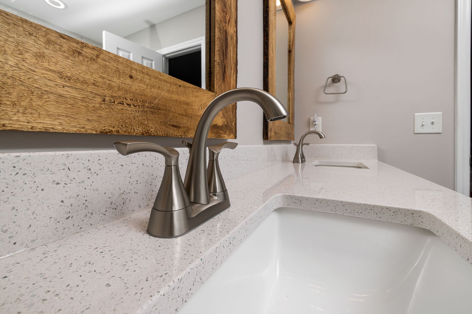 Close-up of a contemporary bathroom sink with a sleek faucet and wooden mirror frame